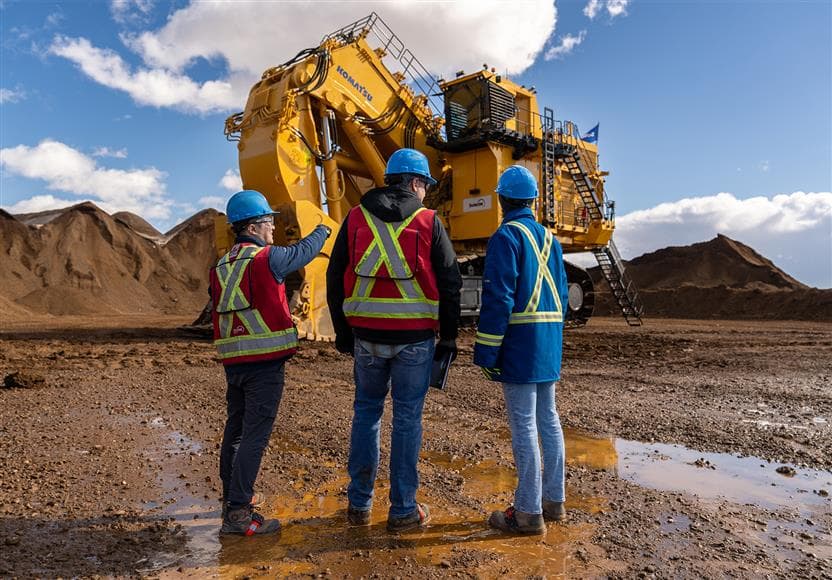 Three Fort Hills employees standing in front of the first PC9000, Komatsu's largest hydraulic shovel commercially available in the world, which was assembled at our Fort Hills mine in March/April 2025 by SMS Equipment. 