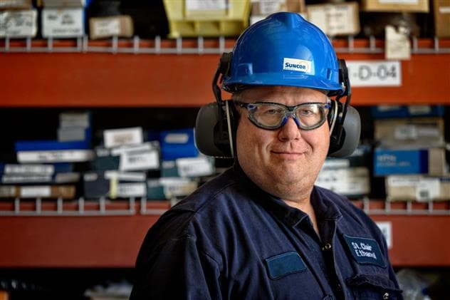 Headshot of a male worker, Greg Robinson, in the Maintenance Building at the St. Clair Ethanol Plant. He is wearing a blue hard hat, safety glasses and coveralls.