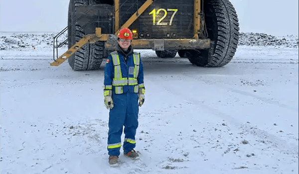 A student standing in front of a truck at the Base Plant site near Fort McMurray. They are wearing PPE and there is snow on the ground.