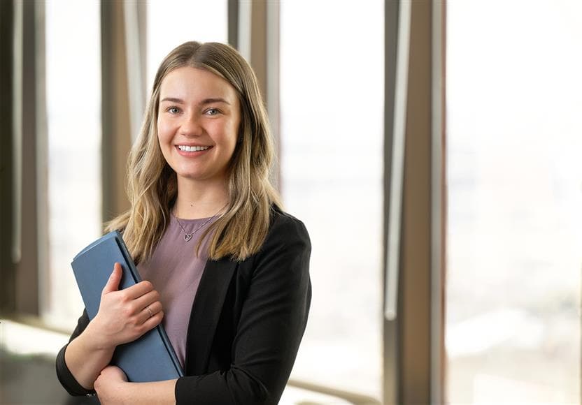 A headshot of a Suncor employee in an office at the Suncor Energy Centre. They are smiling and holding a blue folder.