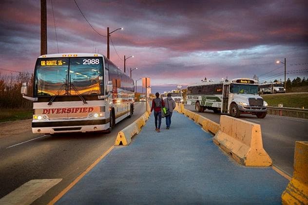 Deux personnes marchant sur une allée vers un autobus à une gare routière. Il y a un coucher de soleil à couper le souffle en arrière-plan. 