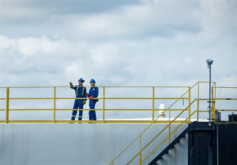 Deux employés debout sur le dessus d'un réservoir de stockage à la raffinerie de Montréal. Ils portent un casque bleu, des lunettes de sécurité, une combinaison et des gants.