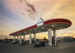 A landscape view of a Petro-Canada gas station. The sky is a blue and yellow sunset with clouds, and vehicles are fueling up.