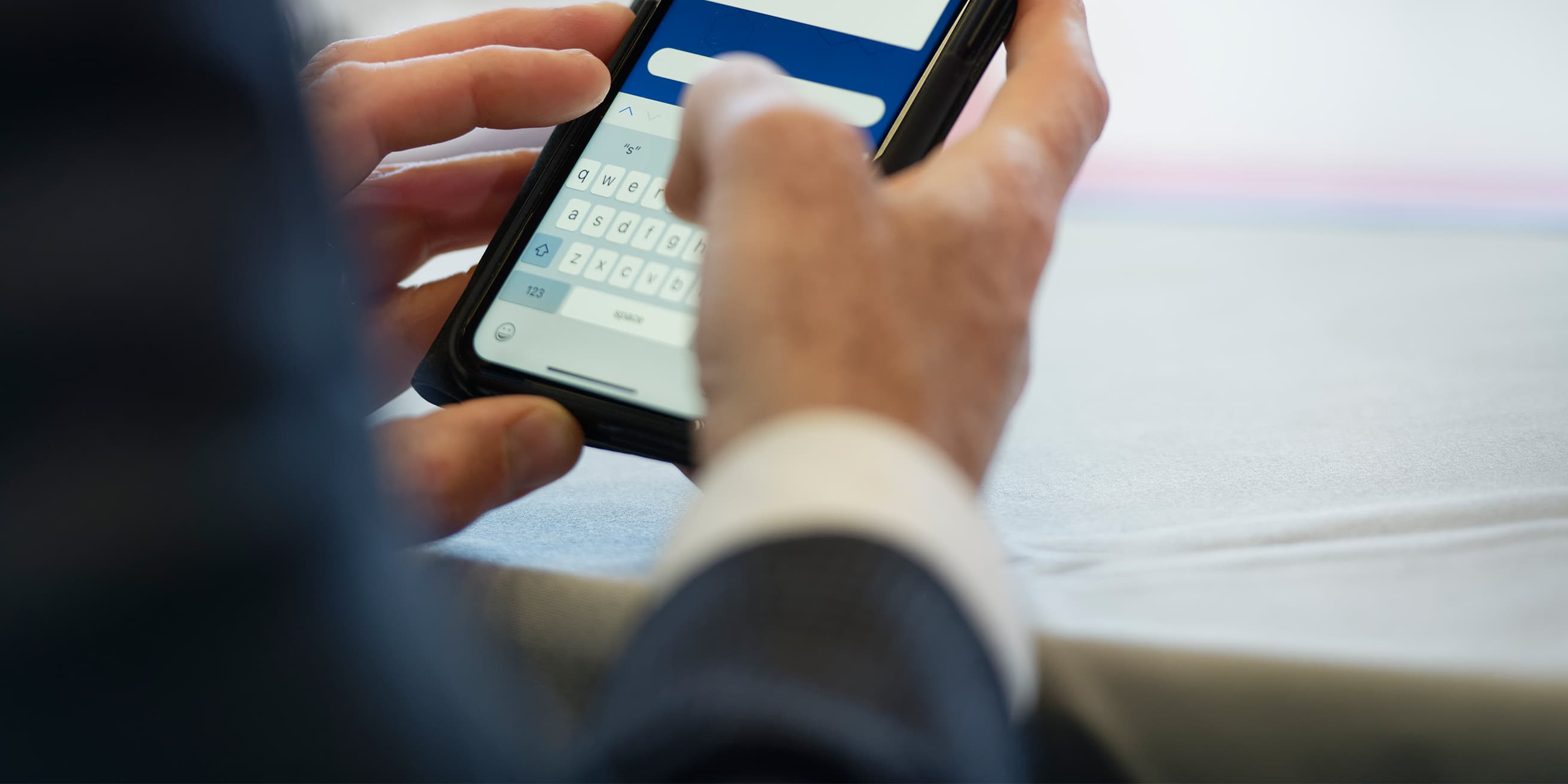 Un homme en complet tient un téléphone cellulaire.