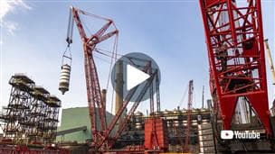 At Suncor’s Base Plant in northern Alberta, a crane lifts a large coke drum during the coke drum integrity project (CDIP), with one of the world's largest ring cranes operated by Mammoet - replacing drums and deck. A large play button appears in the center of the image, with a YouTube logo in the bottom right corner.