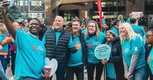 Un groupe de personnes portant des chandails bleus avec la mention « Un grand pas pour les proches aidants » rassemblées pour un autoportrait de groupe à l'extérieur d'un immeuble de bureaux. 