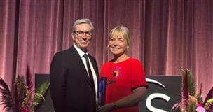 Shelley Powell wearing a red dress and holding an award, stands with Rich Kruger, Suncor’s President and CEO. Rich is wearing a black suite and tie. 