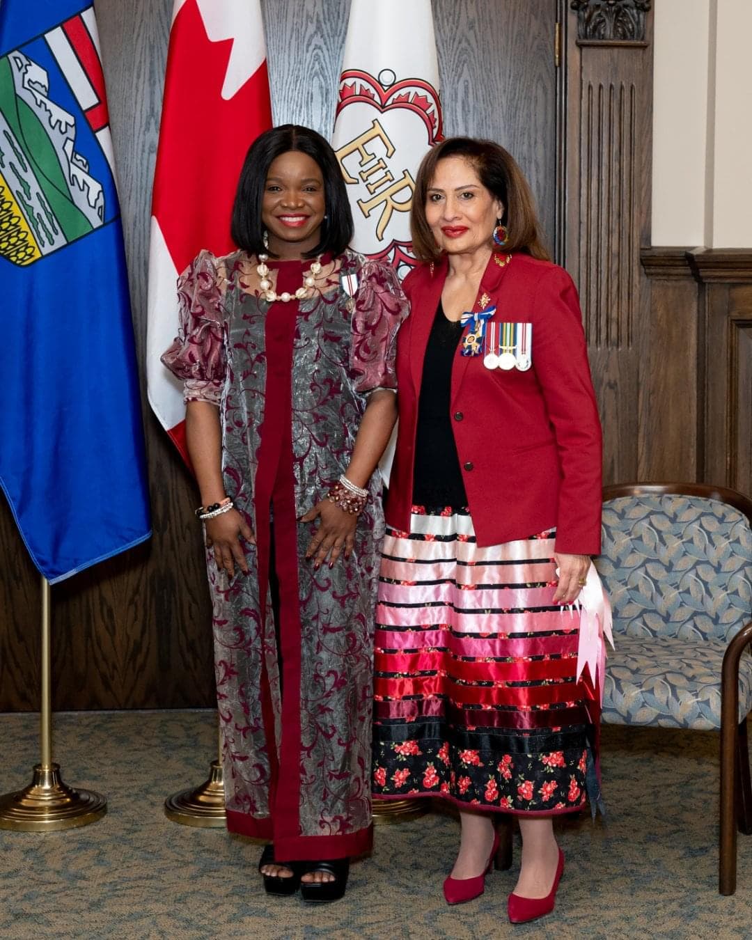 A woman wears a beautiful red dress and smiles receiving her medal. 