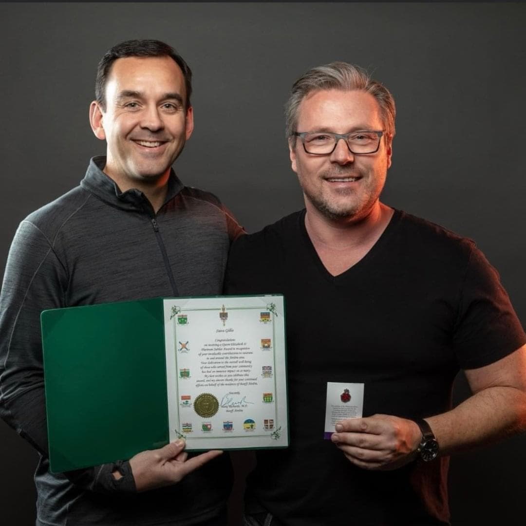 A man with glasses displays his medal pin with a representative. 