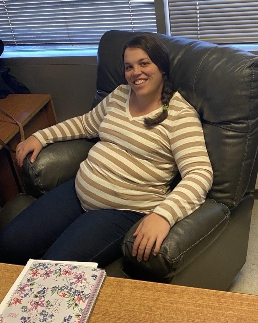 A pregnant woman sits in a comfortable chair in an office.