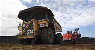 A large, yellow 797 haul truck in an oil sands mine. There is a red shovel behind it and a cloudy sky above.