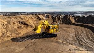 A large, yellow excavator in the dirt at an oil sands mine with blue sky above.