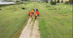 A group of people wearing orange shirts walking down a path. There is green grass and crosses on both sides of the path.