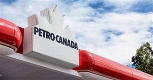 The canopy of a Petro-Canada gas station. There is a red and white sign featuring the Petro-Canada white maple leaf logo and blue sky with clouds above.