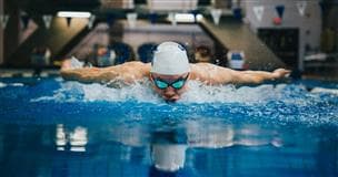 A person swimming in a pool. The swimmer is wearing a white swim cap and goggles. The water if very blue.