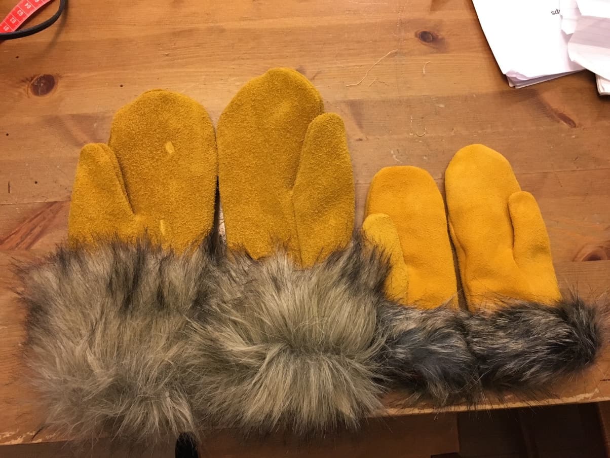 Two pairs of moosehide mittens with fur cuffs on a wooden table.
