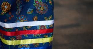 The bottom of dark blue skirt with four ribbons along the hem—white, red, yellow and blue, which are also the colours of the medicine wheel.
