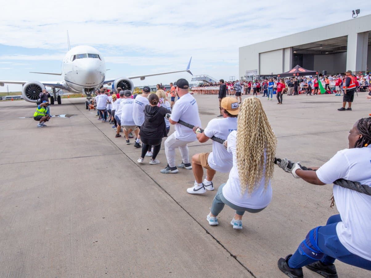 A team of 25 people pulling a plane with a rope across the airport tarmac