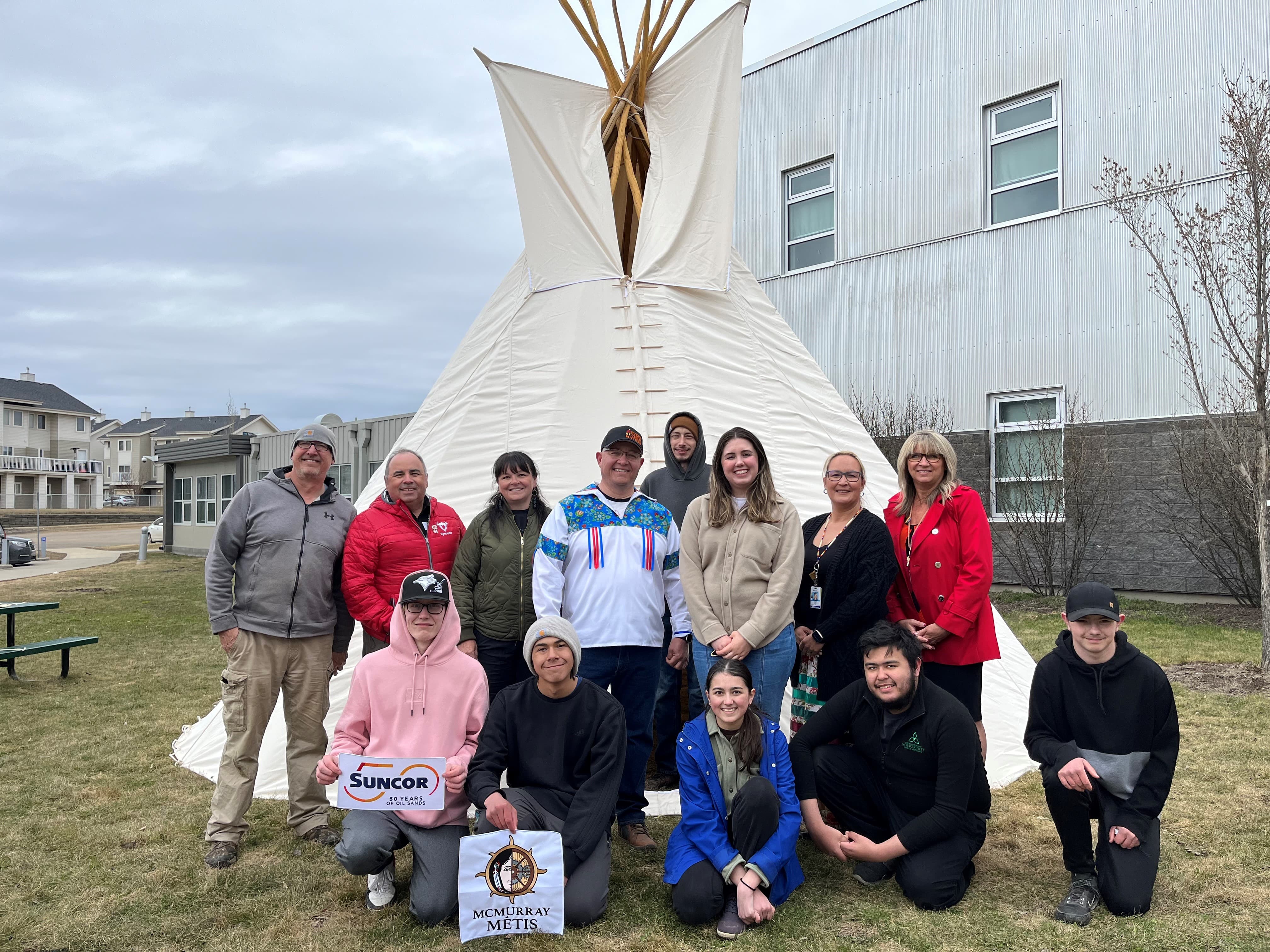 A group of people standing near a teepee outside of a building.