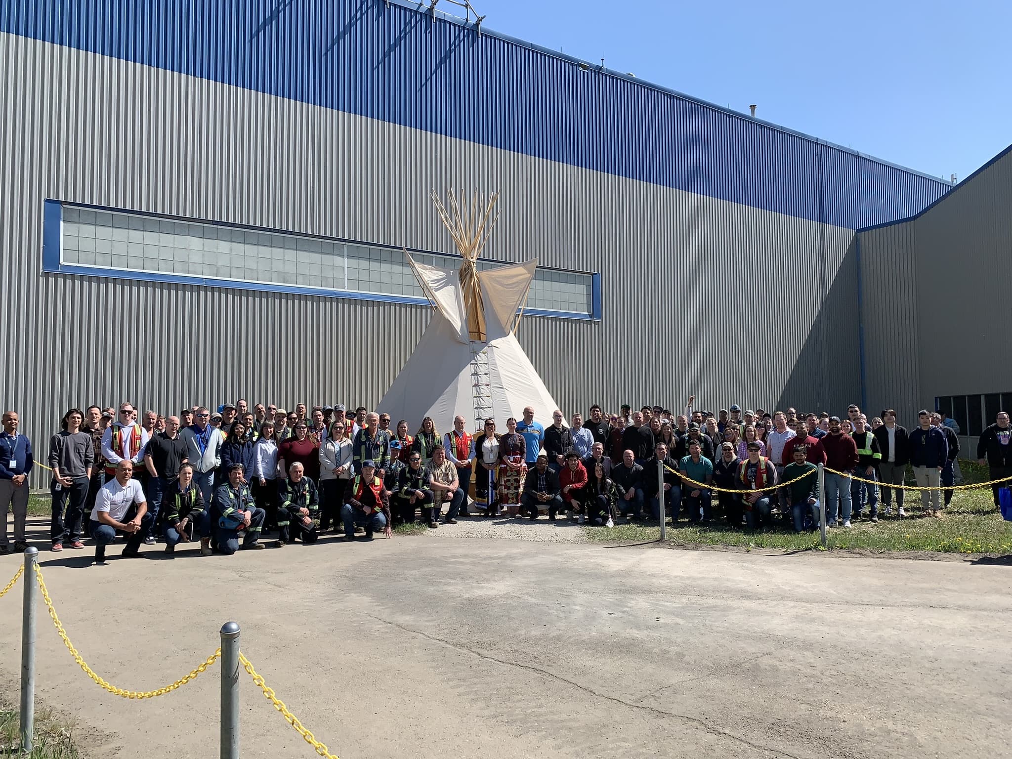 A teepee outside of a building with a large group of people standing around it.
