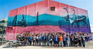 Un groupe de personnes se tient devant un bâtiment sur lequel une murale colorée est peinte.