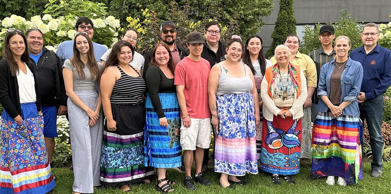 Members of Suncor’s Indigenous Youth Advisory Council stand together outdoors in a garden with several wearing colourful ribbon skirts.