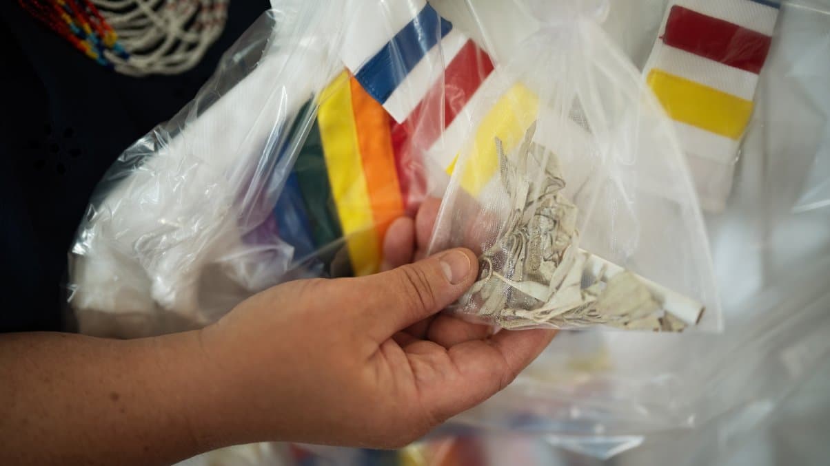 A hand holding a transparent pouch of dried sage and tobacco.