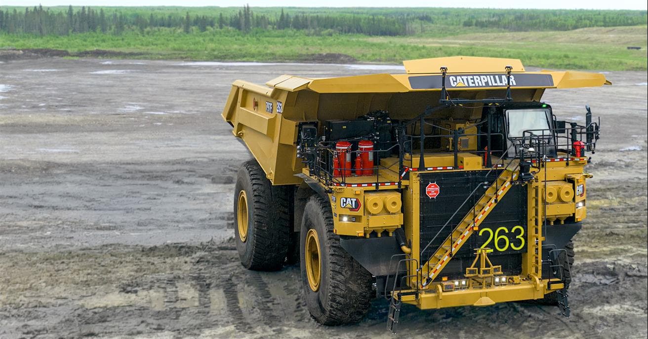 Un camion de transport jaune équipé pour un fonctionnement autonome. Le camion jaune est montré de face devant un paysage minier ouvert, avec un terrain minier au premier plan et un horizon bordé d’arbres en arrière-plan