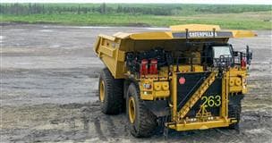 Un camion de transport jaune équipé pour un fonctionnement autonome. Le camion jaune est montré de face devant un paysage minier ouvert, avec un terrain minier au premier plan et un horizon bordé d’arbres en arrière-plan