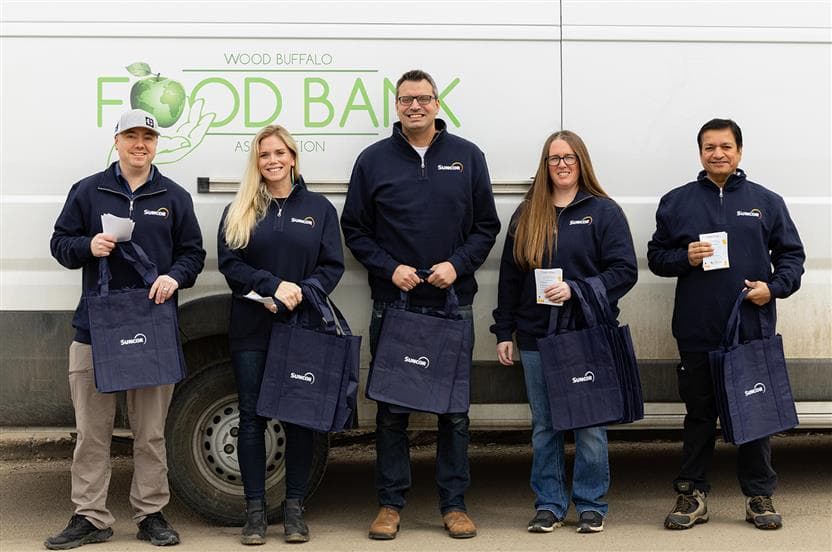 Des bénévoles de Suncor debout à l’extérieur devant un véhicule de la Wood Buffalo Food Bank, tenant des sacs réutilisables avec des articles donnés.
