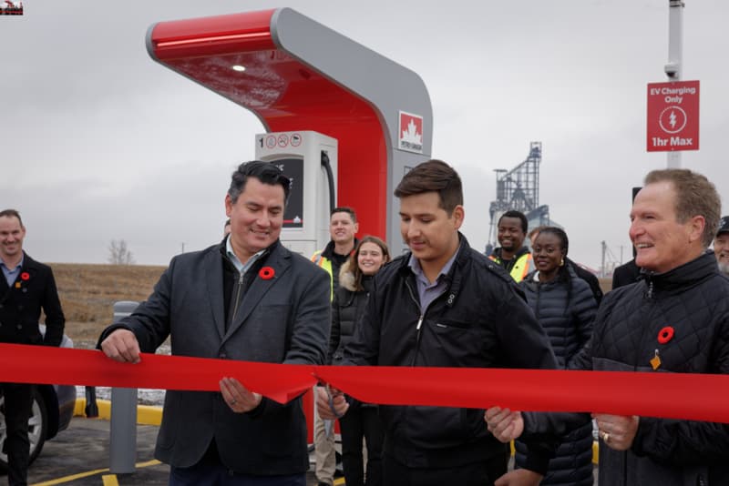 Three men standing in front of a Petro-Canada gas station. One of them is about to cut the red ribbon.