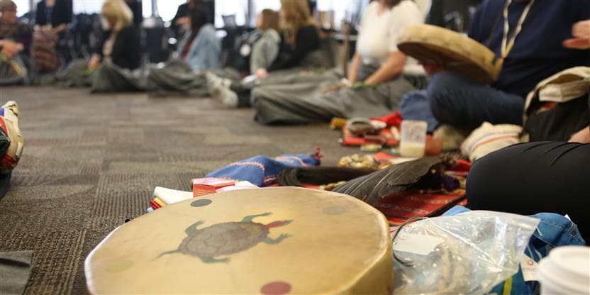 Members of IYAC and the Suncor Support Team sitting in a circle, participating  in a Pipe Ceremony at Suncor Energy Centre for their annual gathering. 
