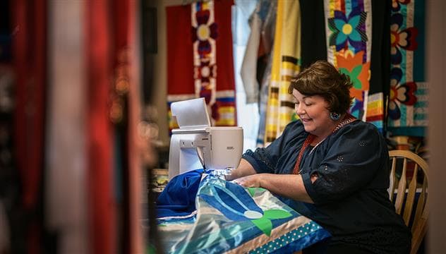 An Indigenous woman sewing a vibrant, colorful ribbon skirt.