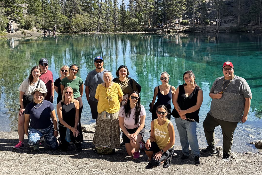 A group of adults and youth pose for a photo in front of a lake.