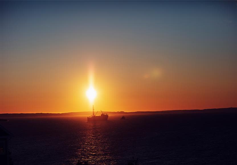 A boat in the distance on the ocean with a dramatic sunset in the background.