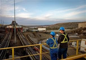 A female and a male worker standing at a railing on the top of Plant 82 Extraction facilities looking out towards the river. They are wearing blue hard hats and safety glasses. 