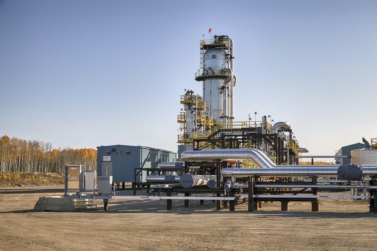 A vertical separator and pipelines at MacKay River Pad 750. There are trees at the edge of the site.