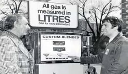 A man stands with a Sunoco attendant at one of the brand-new self-serve gas stations. The man wears a plaid jacket and the employee wears a Sunoco uniform.