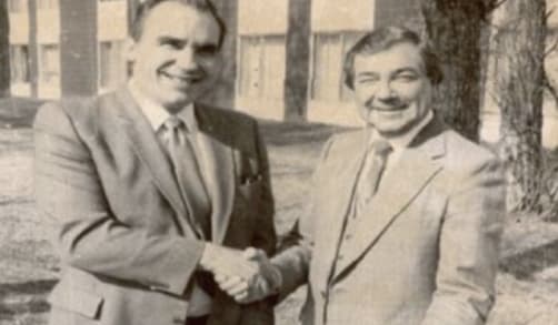 Two men in suits shake hands.