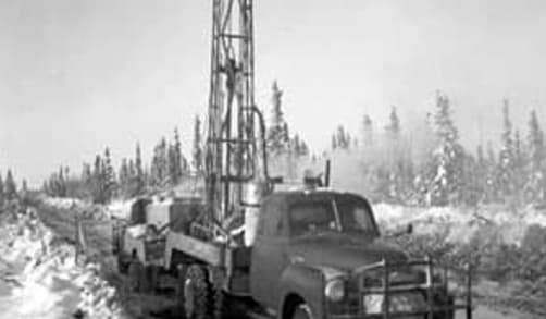 An early oil drilling rig, perched on the back of a truck, is pictured.