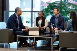 Four employees sit at a table in the Suncor Energy Centre lobby chatting and drinking coffee.