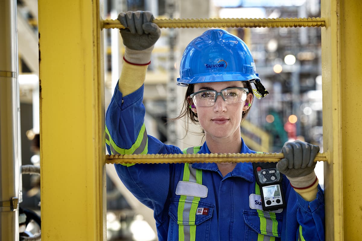 A female worker at the Sarnia Refinery, wearing a blue hard hat, safety glasses, gloves and coveralls
