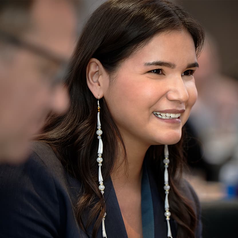 A female Indigenous youth at an Indspire event. She is smiling and is wearing long beaded earrings. 